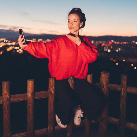 Junge Frau wirft ihrem Handy einen Kussmund zu, hinter ihr ist Barcelona im Dunkeln zu erahnen
