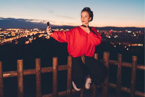 Junge Frau wirft ihrem Handy einen Kussmund zu, hinter ihr ist Barcelona im Dunkeln zu erahnen