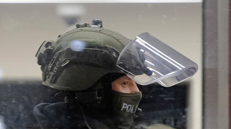 Berlin Polizei Razzia Ein Polizist in grüner Uniform und Sturmhaube unter dem Helm ist mit hochgeklapptem Visier im Profil zu sehen