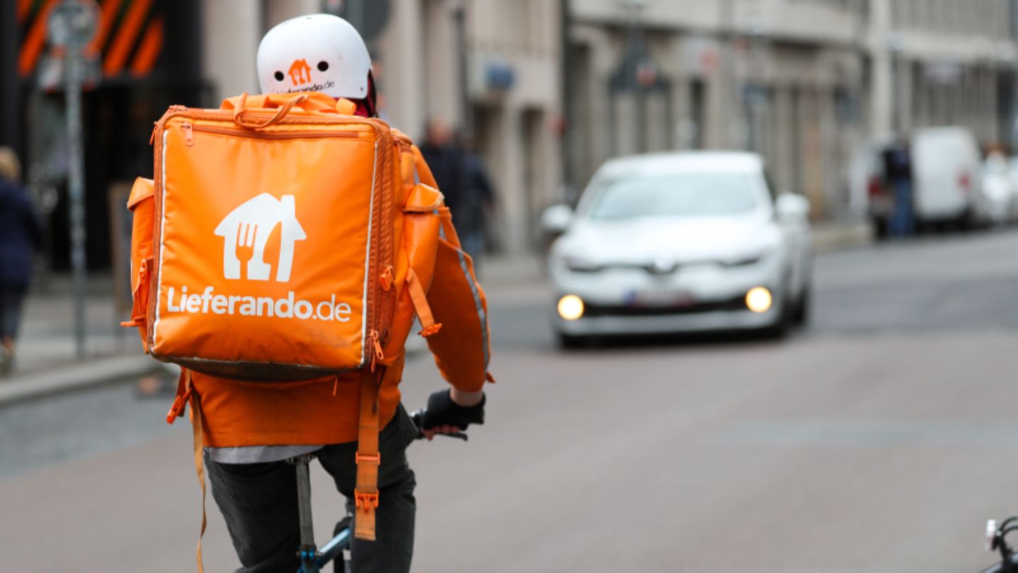 Ein Lieferando-Fahrer in orangefarbener Jacke fährt auf dem Fahrrad
