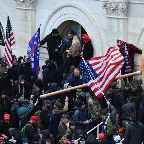 Eine Menschenmenge mit US- und Trump-Flaggen drängt bewaffnet gegen ein weißes Gebäude vor