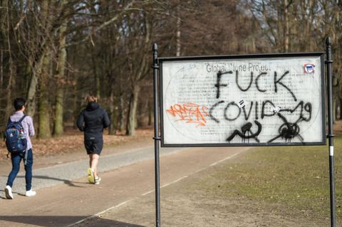 Jogger laufen im Berliner Tiergarten an einem "Fuck Covid"  Schriftzug vorbei