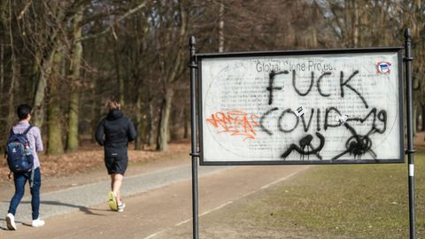 Jogger laufen im Berliner Tiergarten an einem "Fuck Covid"  Schriftzug vorbei