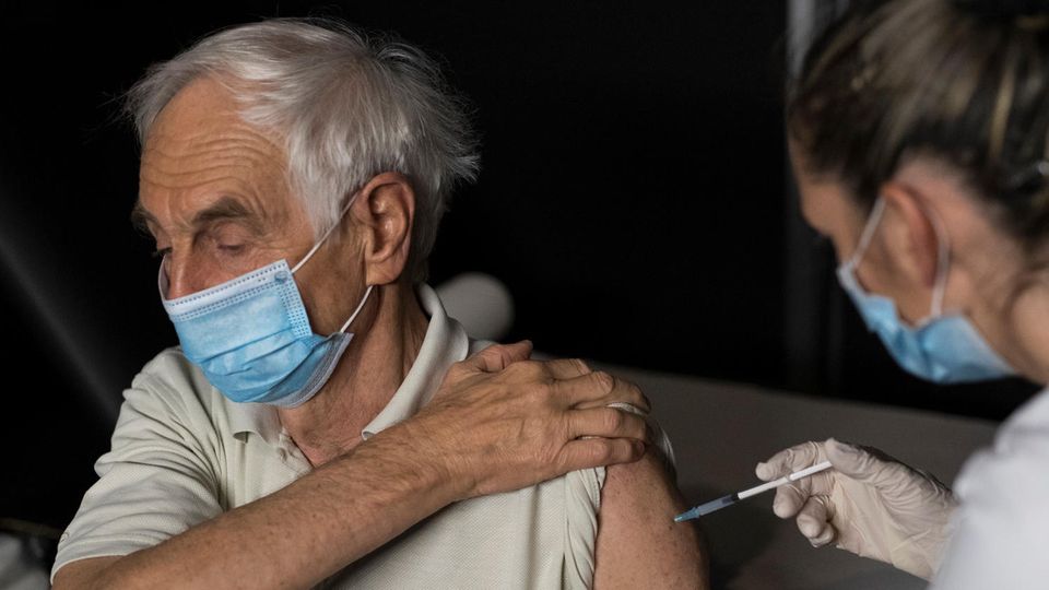Corona Impfung Frankreich Eine Krankenschwester sticht einem älteren, weißhaarigen Mann eine Spritze in den linken Oberarm. Beide tragen OP-Masken