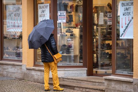 Thüringen, Gotha: Eine Frau steht vor einem geschlossenen Schuhgeschäft und betrachtet die Schuhmodelle