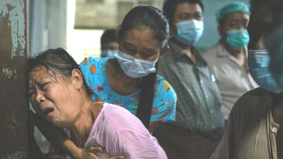 Myanmar Tote Proteste gegen Militärputsch In schwachem Licht lehnt eine mittelalte Asiatin mit von Trauer gezeichnetem Gesicht am Eingangstor eines Krankenhauses