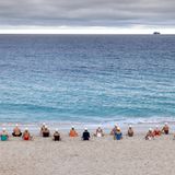 Bild 1 von 7 der Fotostrecke zum Klicken:  Mit Blick auf den Horizont sitzen die Teilnehmer der "lebendige Kunstinstallation" am Meer.