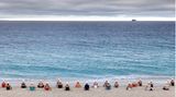 Bild 1 von 7 der Fotostrecke zum Klicken:  Mit Blick auf den Horizont sitzen die Teilnehmer der "lebendige Kunstinstallation" am Meer.