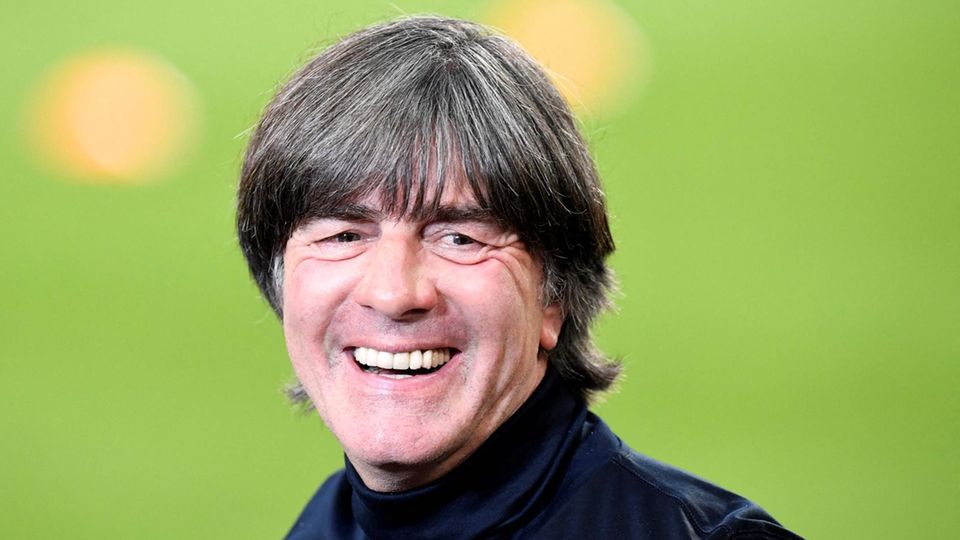 Joachim Löw Jogi Löw In dunkelblauem Rollkragen-Pulli steht Jogi Löw am Rand eines Fußball-Platzes und lacht. Der Rasen im Hintergrund ist unscharf