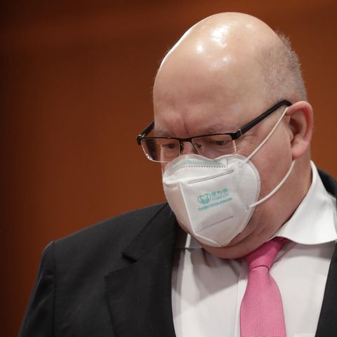 Ein korpulenter Mann mit Halbglatze trägt Brille, FFP2-Maske und einen schwarzen Anzug mit einer rosa Krawatte