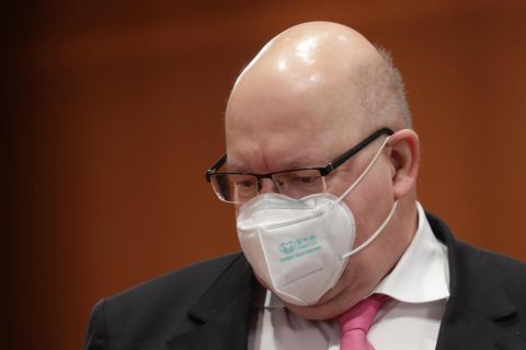 Ein korpulenter Mann mit Halbglatze trägt Brille, FFP2-Maske und einen schwarzen Anzug mit einer rosa Krawatte