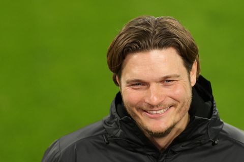 Ein Mann mit dunkelblondem Seitenscheitel grinst, während er auf einem Fußballplatz interviewt wird