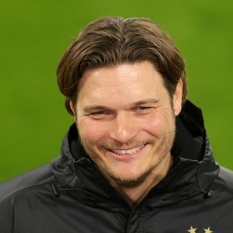 Ein Mann mit dunkelblondem Seitenscheitel grinst, während er auf einem Fußballplatz interviewt wird