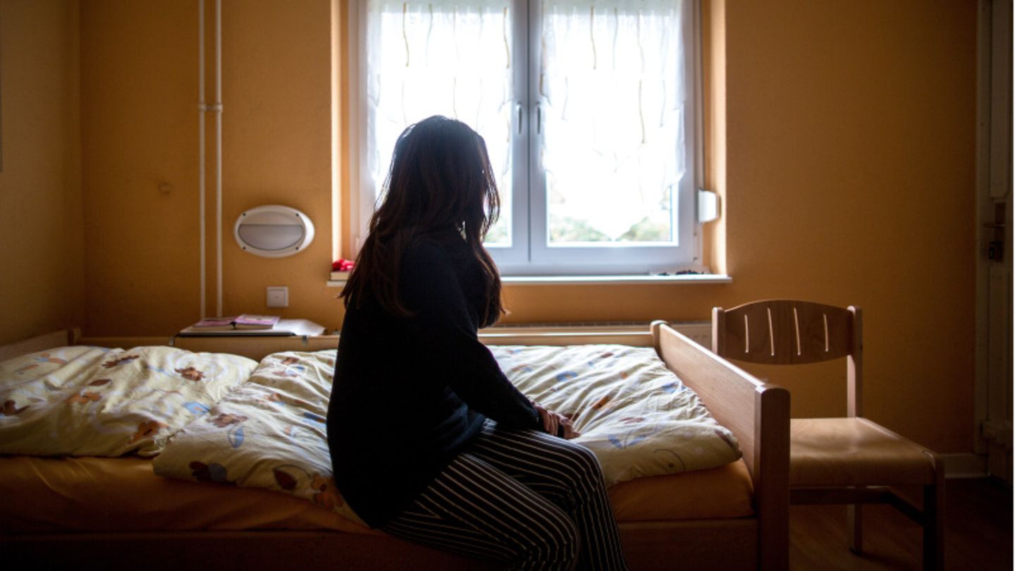 Eine Frau sitzt in einem Frauenhaus auf einem Bett und schaut zum Fenster