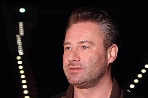 Ein Mann mit dunkelblonder Tolle steht in einer dunklen Arena, in der nur sein Gesicht ausgeleuchtet ist