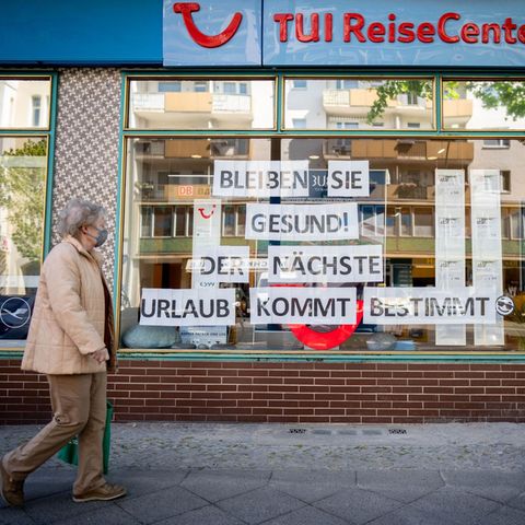 Eine Passantin mit Maske geht an einem Reisebüro vorbei