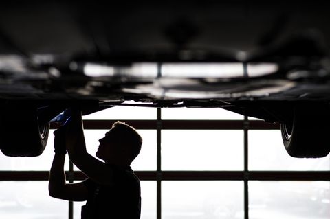 Mechaniker arbeitet in einer KfZ-Werkstatt an der Unterseite eines Autos.