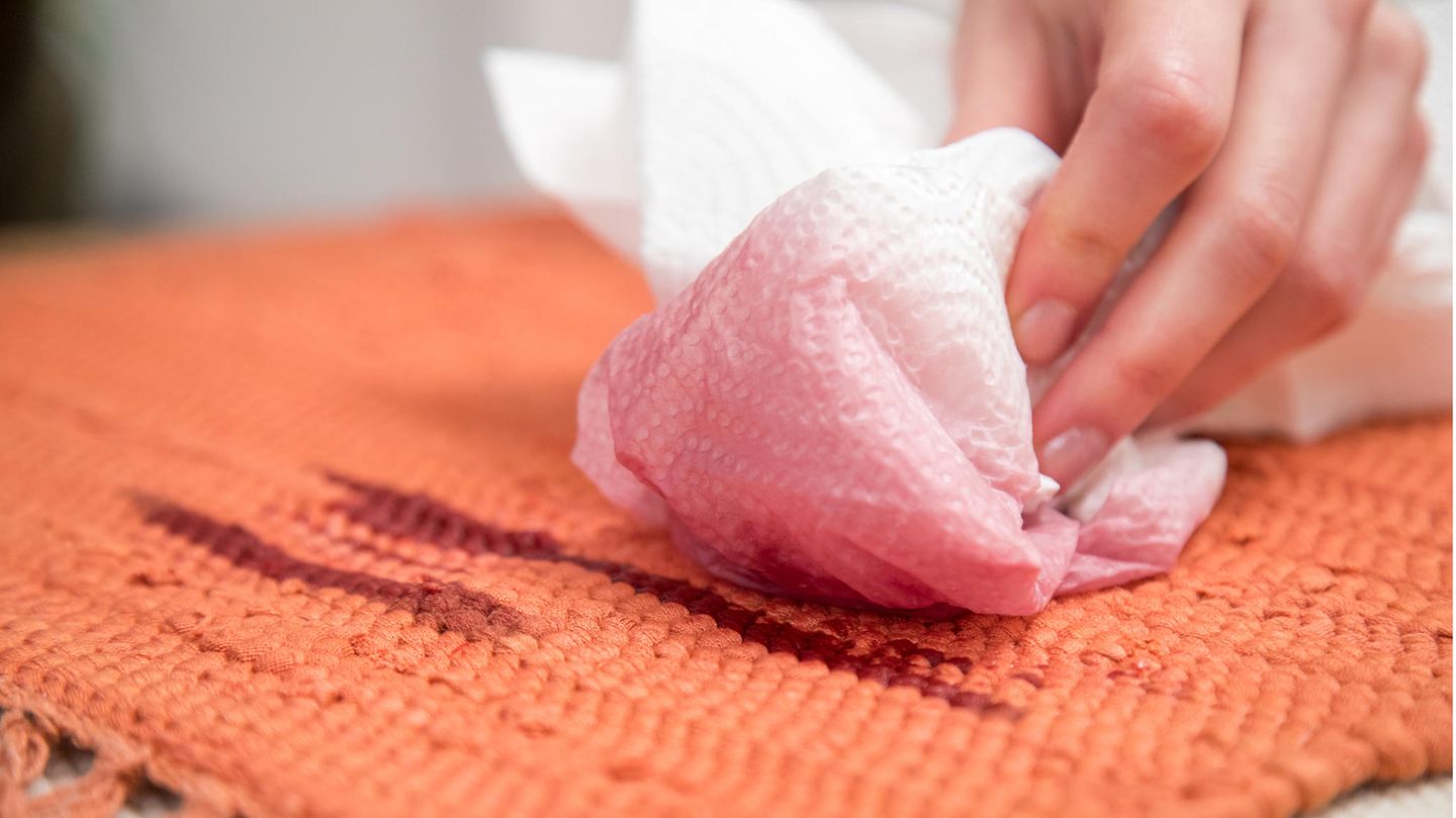 Frau tupft Rotweinfleck mithilfe eines Küchenpapiers aus einem Teppich.