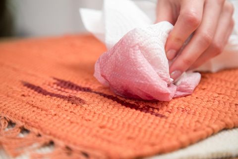 Frau tupft Rotweinfleck mithilfe eines Küchenpapiers aus einem Teppich.