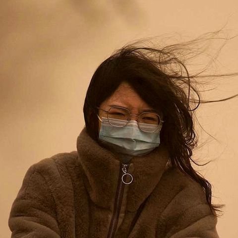 Eine junge Chinesin mit langen schwarzen Haaren fährt mit OP-Maske durch den Sandsturm, der den Himmel gelb einfärbt