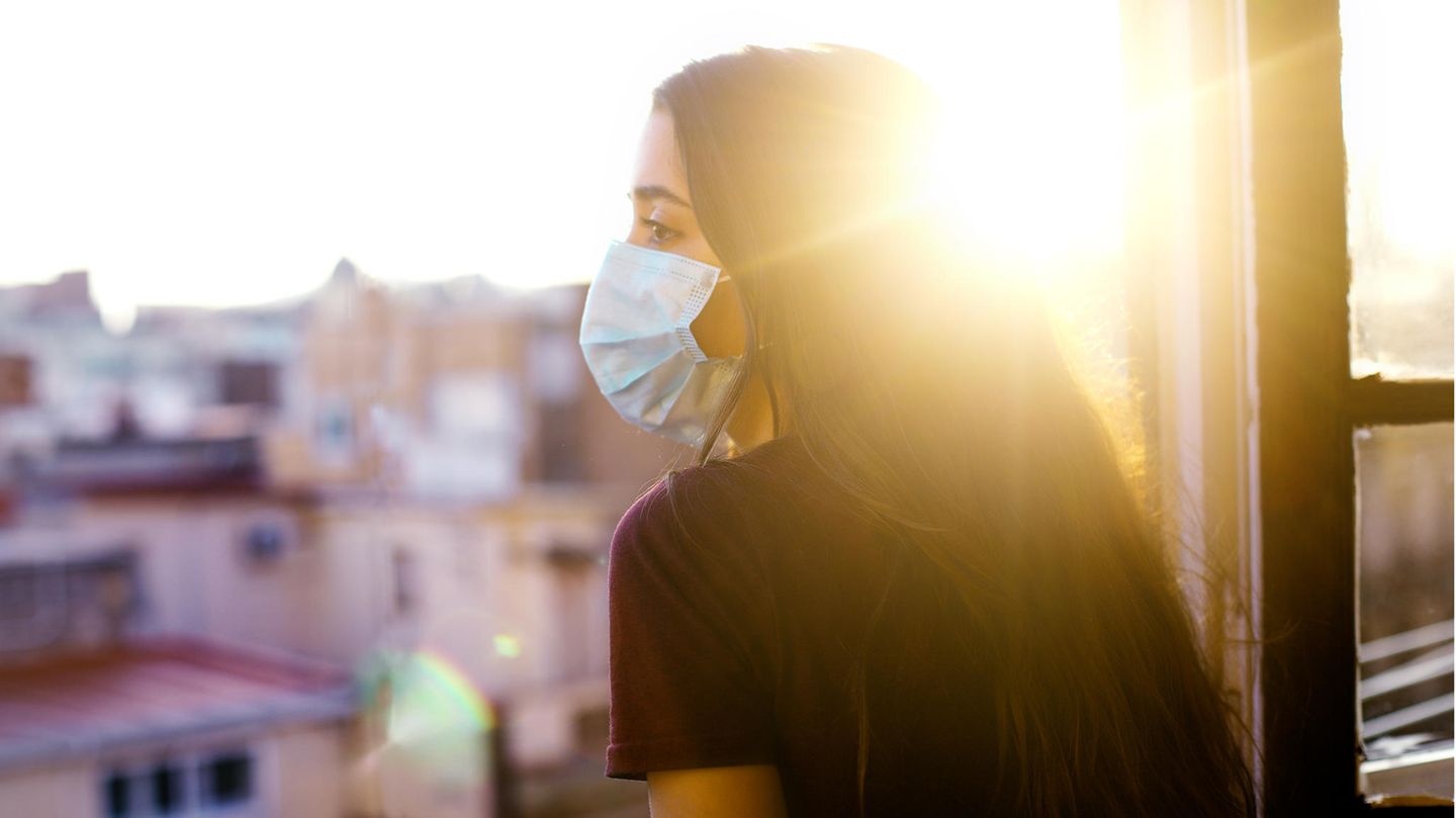 Frau mit Maske am Fenster im Sonnenschein