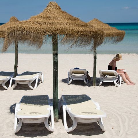  Eine Urlauberin sitzt am Strand an der Platja de Muro auf Mallorca