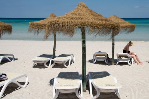  Eine Urlauberin sitzt am Strand an der Platja de Muro auf Mallorca