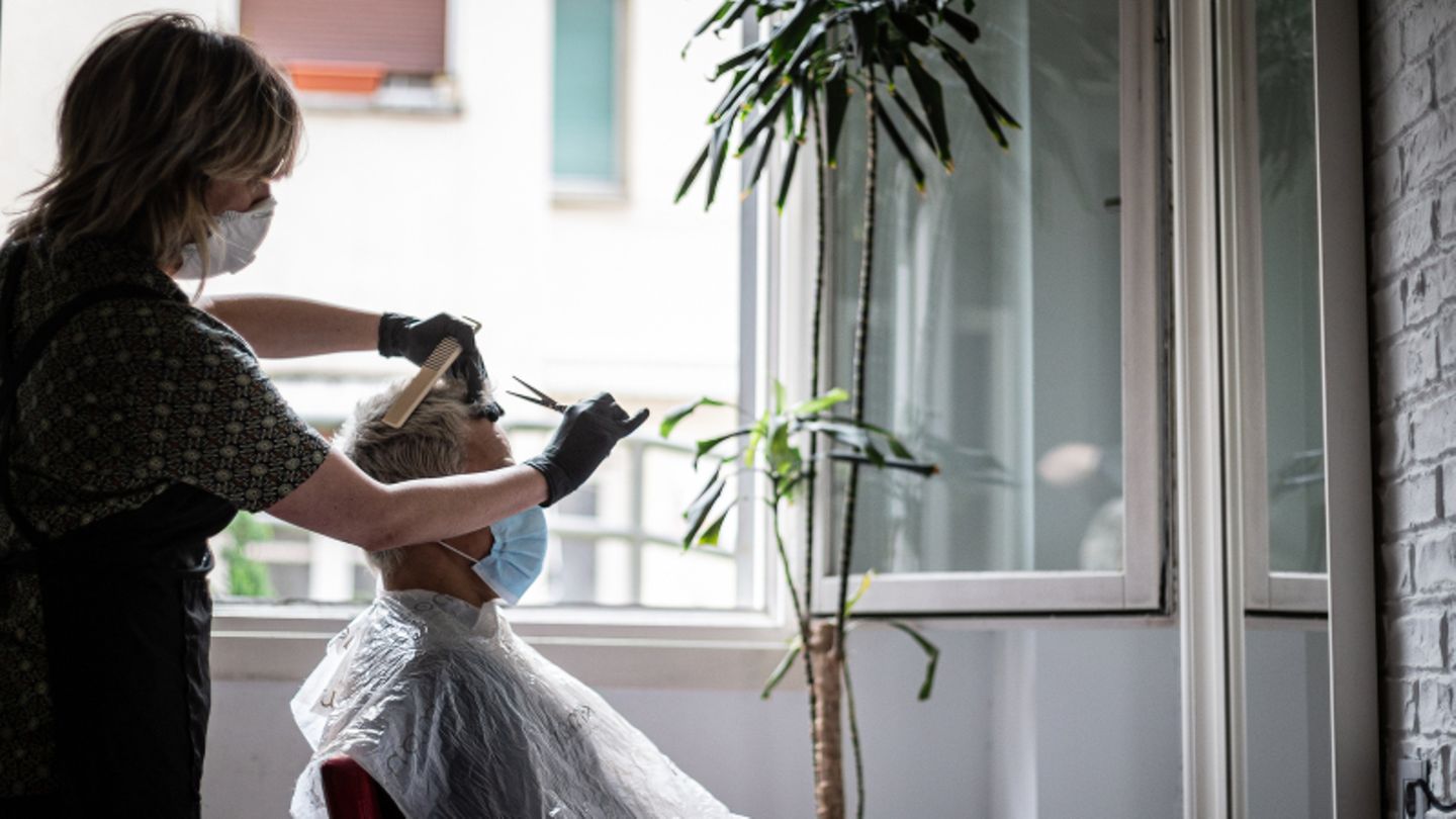 Eine Friseurin schneidet einem Mann die Haare, beide tragen einen Mundschutz