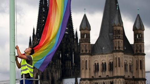 Ein Arbeiter hängt vor der Kulisse des Kölner Doms und der Kirche Groß St. Martin eine Regenbogenfahne auf