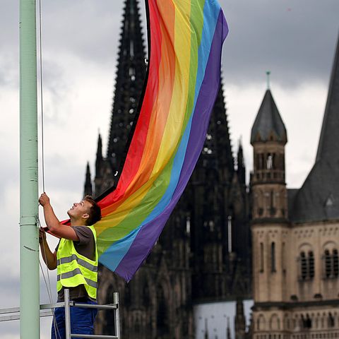 Ein Arbeiter hängt vor der Kulisse des Kölner Doms und der Kirche Groß St. Martin eine Regenbogenfahne auf