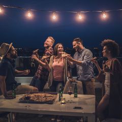 Balkonbeleuchtung: Eine Gruppe junger Menschen feiert in der Nacht auf dem Balkon unter einer Lichterkette
