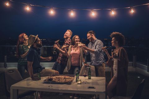 Balkonbeleuchtung: Eine Gruppe junger Menschen feiert in der Nacht auf dem Balkon unter einer Lichterkette