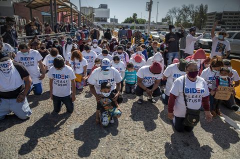 Eine Gruppe Migranten kniet am US-Grenzübergang und betet. Auf ihren T-Shirts steht: "Biden, lass uns bitte rein"