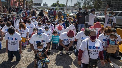 Eine Gruppe Migranten kniet am US-Grenzübergang und betet. Auf ihren T-Shirts steht: "Biden, lass uns bitte rein"