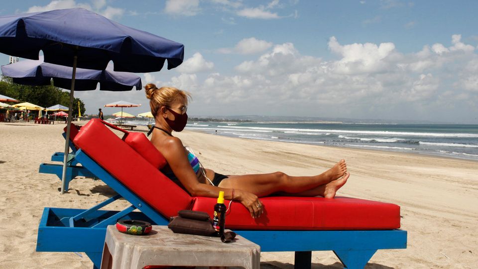 Eine Frau sonnt sich im Bikini auf einer blauen Strandliege mit dicker roter Auflage