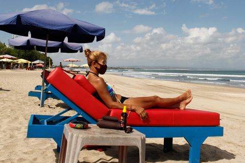 Eine Frau sonnt sich im Bikini auf einer blauen Strandliege mit dicker roter Auflage