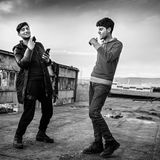 "Diese beiden Männer sind Cousins. Der Linke heißt Zeeshan Akash Khan und ist auf dem Bild 20 Jahre alt, der Rechte ist Ikham Khan, 17 Jahre alt. Sie kommen aus Pakistan. Sie stehen hier auf demselben Vordach, auf dem ich die Männer auf dem vorhergehenden Bild beim Kochen fotografiert hatte. Diese beiden nutzten diesen Ort um sich ein bisschen zu vergnügen. Zeeshan spielte Hochzeitsmusik auf dem Handy und sie tanzten dazu.  Während der Zeit, die ich in Bihac verbrachte, begegnete ich Zeeshan und Ikham mehrmals. Und wann immer ich sie traf, waren sie guter Laune. Das war auffällig und es hat mich beeindruckt. Irgendwann habe ich sie gefragt: "Warum seid Ihr so gut drauf? Eure Lage ist ja nicht gerade rosig." Da hat Zeeshan geantwortet: "Was soll ich denn sonst tun? Ich mag nicht immer schlechte Laune haben."  Bei diesem Bild geht es mir darum zu zeigen, wie diese Menschen versuchen, ihre Würde zu wahren. Nicht zu vergessen, wie sie sich selbst sehen – ungeachtet der Umstände, in denen sie gerade leben. Natürlich wissen Zeeshan, Ikham und all die anderen Flüchtenden, wie schlecht ihre Lage ist. Trotzdem achten diese beiden auf ihren Style. Einen von ihnen hatte ich kurz vorher getroffen, als er sich gerade die Haare schneiden ließ. Die beiden lassen sich nicht auf die Umgebung reduzieren, in der sie dort gerade stecken. Aus diesem Bild spricht für mich ein unbedingter Durchhaltewillen. Es sagt: 'Seht her, wir sind mehr als das, was die Flucht aus uns macht.'"