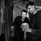 "Der Mann mit dem Handy in der Hand ist Habib Hazrat. Auf dem Bild telefoniert er gerade per Videochat mit seiner dreijährigen Tochter zu Hause in Pakistan. Sie hatte verlangt, mit seinem Zimmergenossen Nursaid zu sprechen, darum hielt er ihm das Handy hin. Habibs Kinder bitten ihn häufig, zurück nach Hause zu kommen.  Mit vielen der Menschen, die ich in Bosnien getroffen habe, versuche ich seither Kontakt zu halten. Habib hat es in die EU geschafft. Eine Weile lang war er in Deutschland. Inzwischen lebt er in einer Kleinstadt in Nord-Italien. Er versucht, dort irgendwelche Papiere zu ergattern, damit er legal arbeiten darf. Denn er möchte seine Frau und seine Kinder zu sich holen.  Die Aufnahme ist im ehemaligen Bürotrakt der kaputten Fabrik in Bihac entstanden. Im einzigen Raum des Gebäudes, dessen Fenster noch intakt waren. Zehn Männer teilten ihn sich als Schlafplatz. Nachts breiteten sie Decken auf dem blanken Boden aus. Tagsüber fegten sie den Raum immer wieder, damit er möglichst sauber blieb."