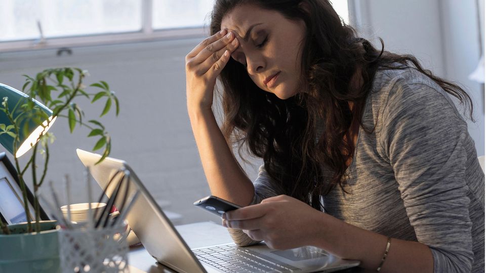 Geschäftsfrau schaut frustriert auf Smartphone und Laptop