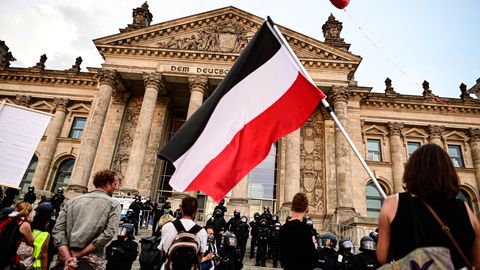 Teilnehmer einer Kundgebung gegen die Corona-Maßnahmen stehen vor dem Reichstag, ein Teilnehmer hält eine Reichsflagge