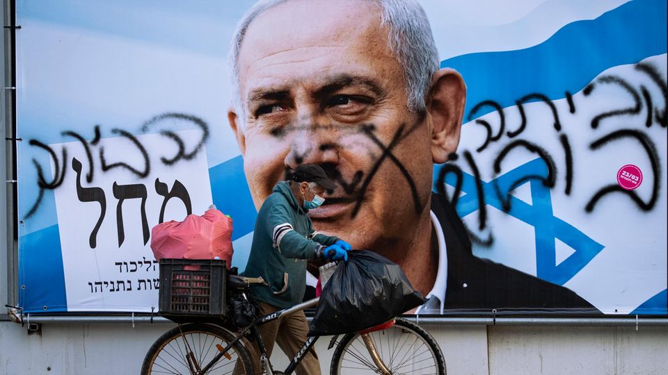 Ein Mann schiebt ein Fahrrad an einem beschmierten Wahlkampfplakat der Likud-Partei vorbei