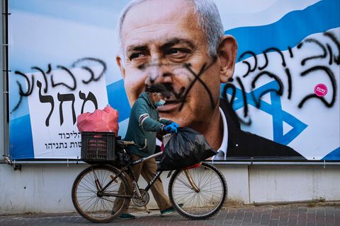 Ein Mann schiebt ein Fahrrad an einem beschmierten Wahlkampfplakat der Likud-Partei vorbei