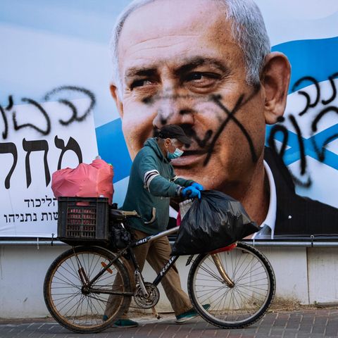 Ein Mann schiebt ein Fahrrad an einem beschmierten Wahlkampfplakat der Likud-Partei vorbei