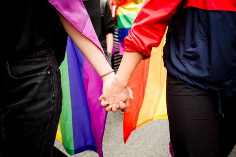 Ein homosexuelles Paar hält Hände vor einer Regenbogenflagge.