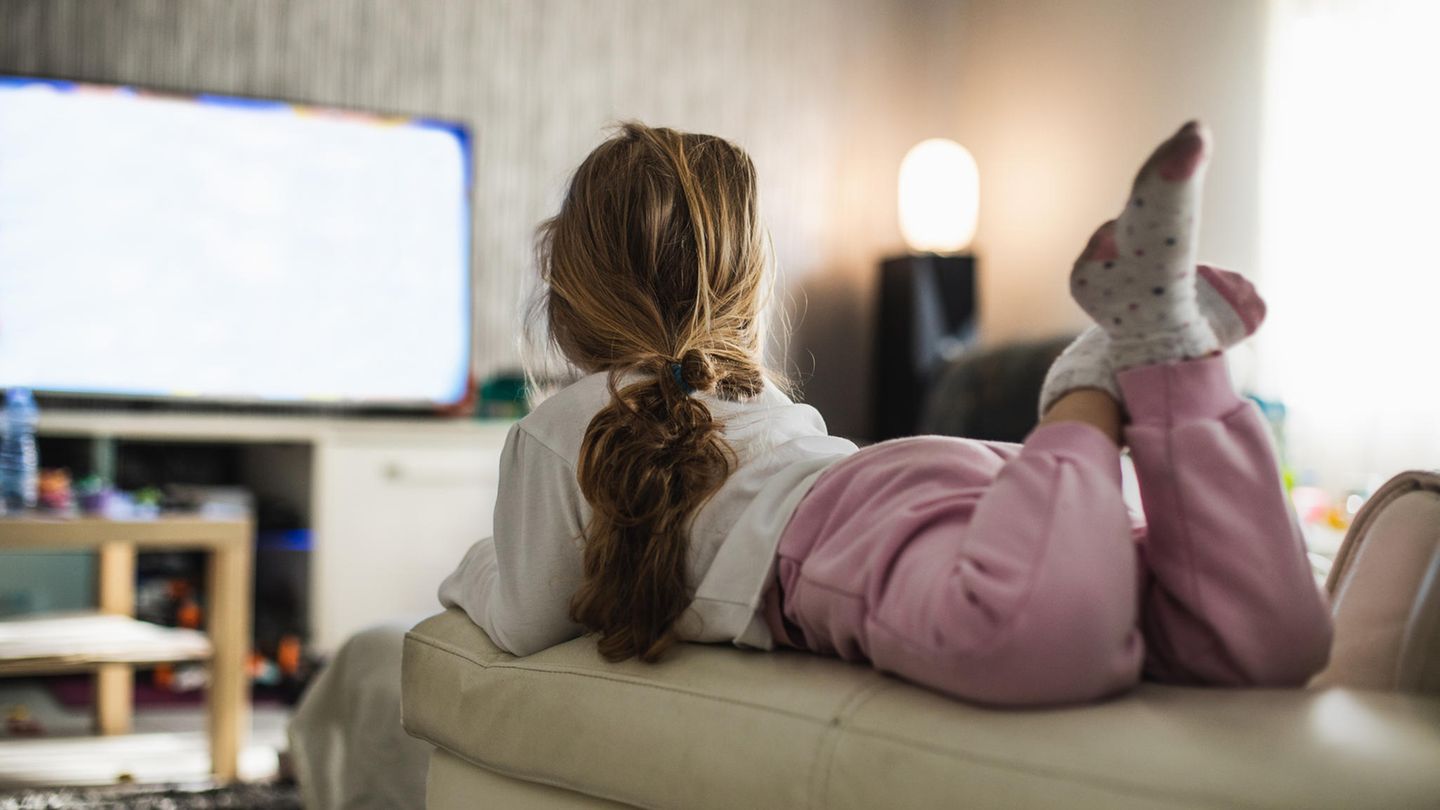 Mädchen liegt auf einer Couch und schaut Fernsehen
