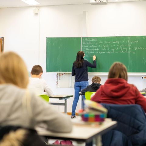 Schüler sitzen im Unterricht, während eine Lehrerin an die Tafel schreibt