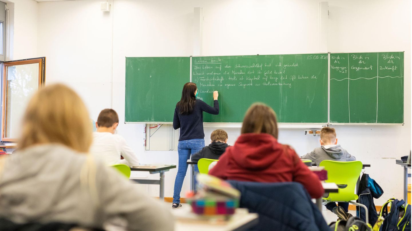Schüler sitzen im Unterricht, während eine Lehrerin an die Tafel schreibt