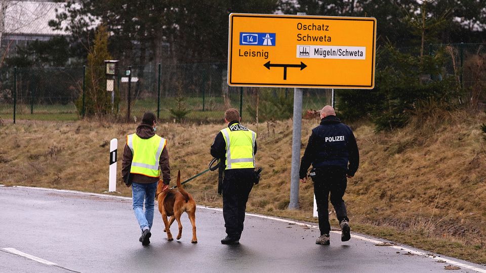 Nachrichten Deutschland Mügeln Polizisten laufen mit einem Polizeihund an einer Straße in der Nähe des Fundorts einer Babyleichte