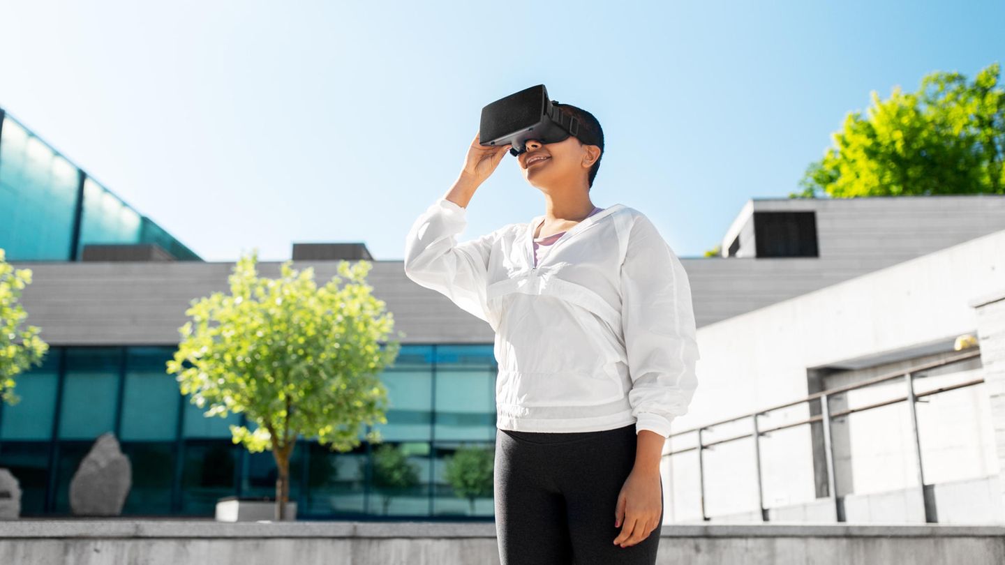 Eine Person trägt eine Virtual Reality-Brille und steht vor einem Haus