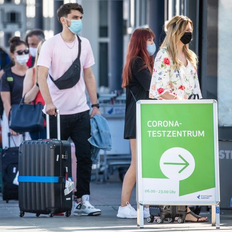 Reiserückkehrer aus Spanien stehen mit Mundschutz vor dem Corona-Testzentrum am Flughafen Stuttgart an